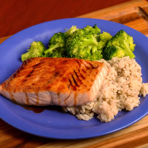 Grilled salmon with a glaze, served with white rice and steamed broccoli on a blue plate.