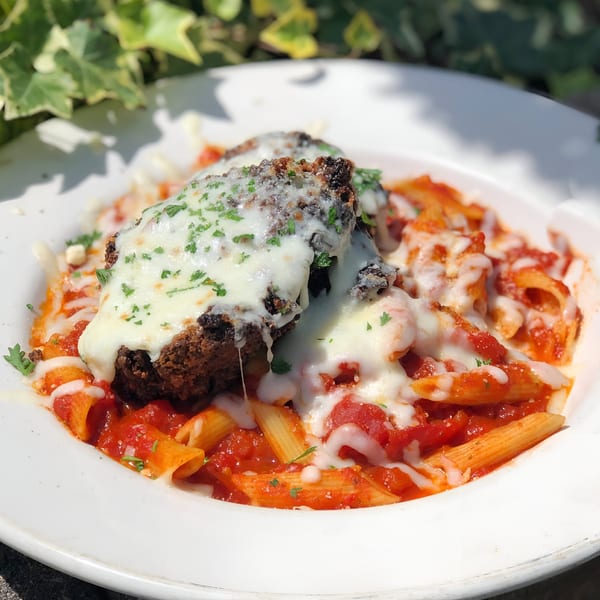 Meatloaf with melted mozzarella cheese and penne pasta in red sauce, garnished with parsley.
