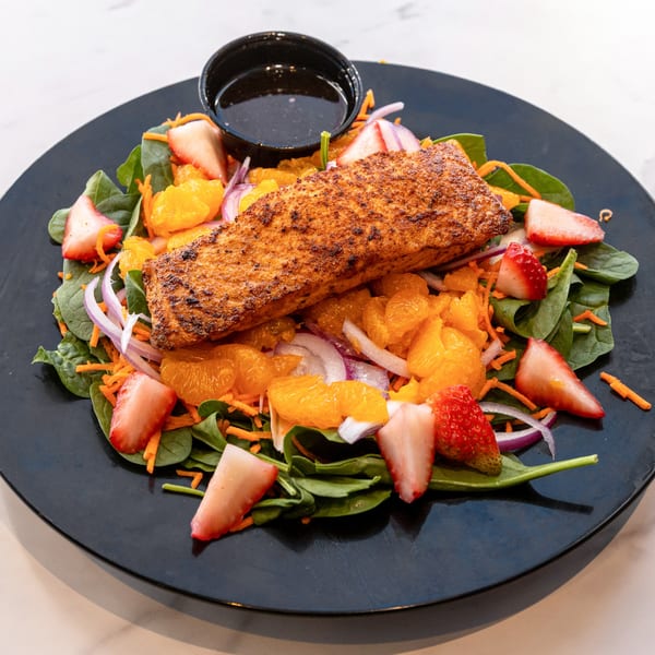 Grilled salmon salad with spinach, mandarin oranges, strawberries, red onion, and shredded carrots.