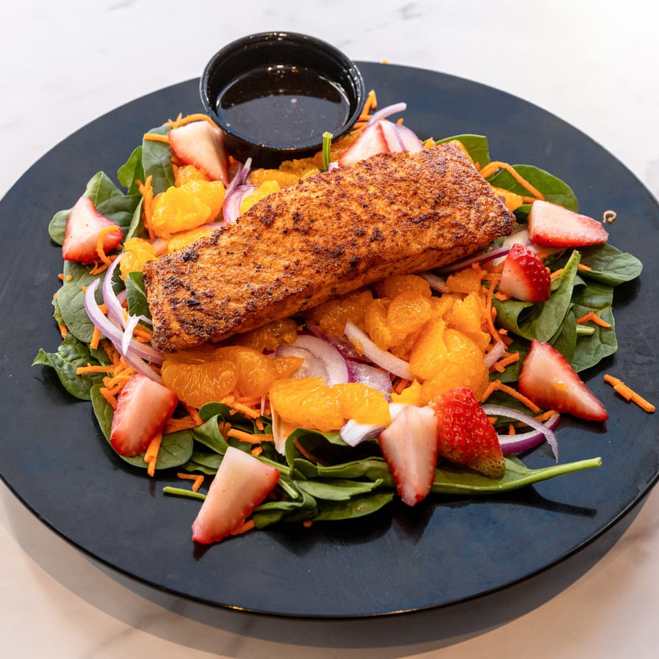 Grilled salmon salad with spinach, mandarin oranges, strawberries, red onion, and shredded carrots.
