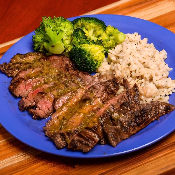 Grilled steak with green sauce, broccoli, and rice on a blue plate at Dilworth Neighborhood Grille.