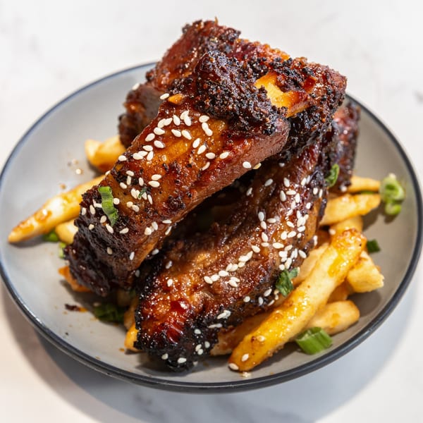 Sweet and spicy ribs with sesame seeds and french fries on a gray plate at Dilworth Neighborhood Grille.