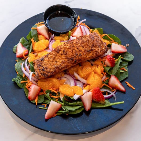 Grilled salmon salad with spinach, strawberries, mandarin oranges, red onion, and dressing on a black plate.