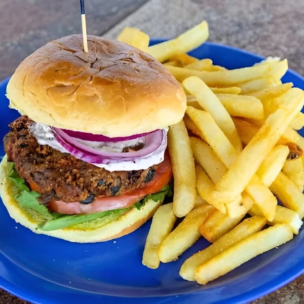 A Dilworth Neighborhood Grille black bean burger with red onion, tomato, lettuce, and fries on a blue plate.